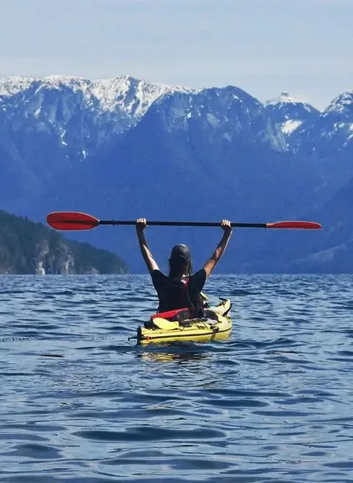 Adrianne kayaking on a calm lake surrounded by mountains, reflecting balance, resilience, and connection with nature