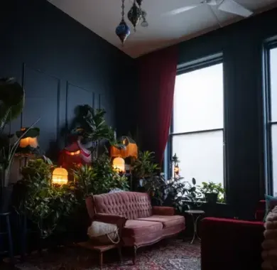 Therapy room with a pink loveseat, tall window, soft lighting, and indoor plants.